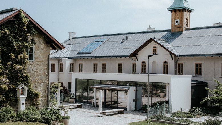 Ein modernes Gebäude mit Solarpanelen auf dem Dach und einem Uhrturm, umgeben von Grünflächen.
