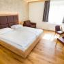 Modern eingerichtetes Hotelzimmer mit Doppelbett, Schreibtisch, St&uuml;hlen und einem Sessel.