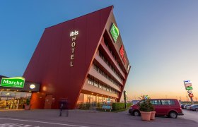 Modernes Hotelgeb&auml;ude mit schr&auml;ger Fassade und Leuchtschrift 'ibis HOTEL'.