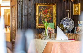 Gem&uuml;tlich gedeckter Tisch in einem rustikalen Restaurant mit Blumenbild und Dekorationen an der Wand.