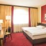 Ein gem&uuml;tliches Hotelzimmer mit Doppelbett, rotem Teppich, Schreibtisch, Fernseher und moderner Kunst an der Wand.
