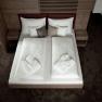 Ein modernes Hotelzimmer mit einem Doppelbett, wei&szlig;en Bettdecken und Badem&auml;nteln, umgeben von Holzm&ouml;beln.