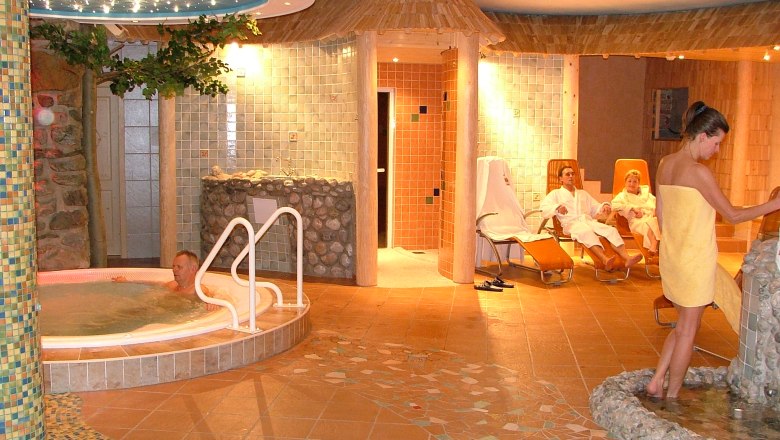 Ein Wellnessbereich mit Whirlpool, Liegestühlen und Personen in Bademänteln.