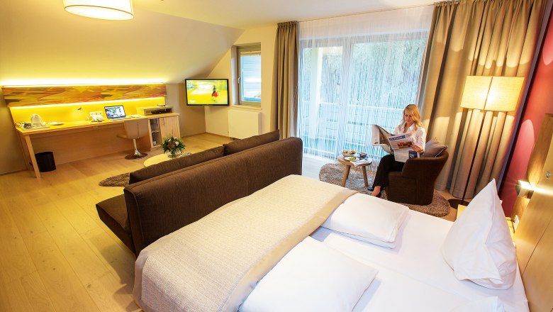 Modernes Hotelzimmer mit Doppelbett, Schreibtisch, Fernseher und Frau, die Zeitung liest.