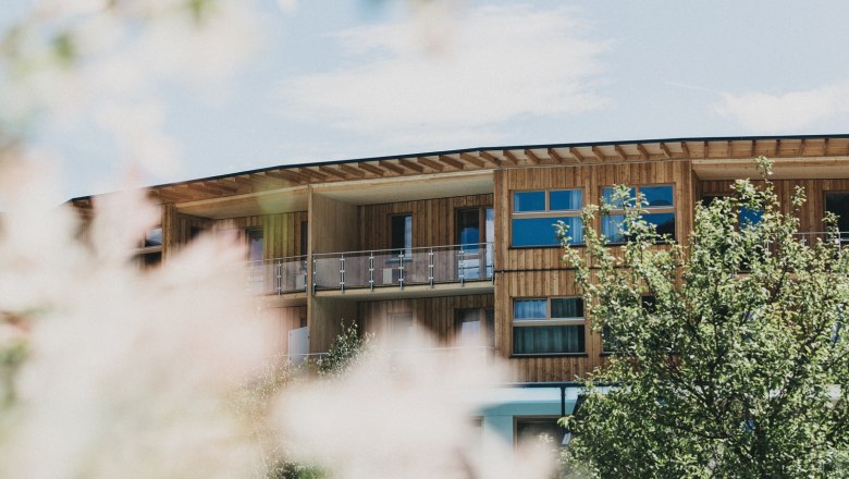 Holzgebäude des Naturhotels Molzbachhof mit Bäumen im Vordergrund.