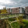 Glas&uuml;berdachter &Uuml;bergang zwischen Therme Laa und Hotelgeb&auml;ude, umgeben von gr&uuml;ner Landschaft.