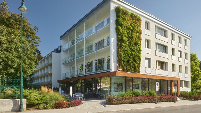 Moderne Gebäudeaußenansicht mit vertikalem Garten und Glasbalkonen bei Tageslicht.
