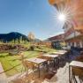 Terrasse des JUFA Hotels Annaberg mit Tischen, St&uuml;hlen und Spielplatz im Hintergrund bei Sonnenschein.