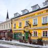 Au&szlig;enansicht eines gelben Geb&auml;udes mit der Aufschrift 'Hotel-Restaurant zur Post' im Winter, umgeben von Schnee und dekoriert mit Lichtern.