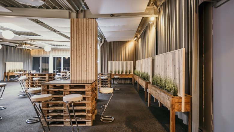 Innenansicht des Foyers der ARENA NOVA Kongresshalle mit modernen Möbeln aus Paletten und Pflanzen.