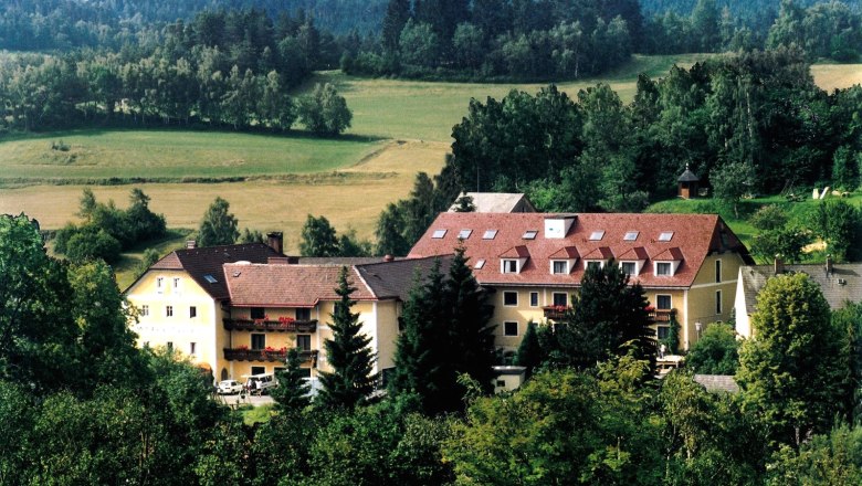 Ein gro&szlig;es Geb&auml;ude mit roten D&auml;chern in einer gr&uuml;nen, bewaldeten Landschaft.