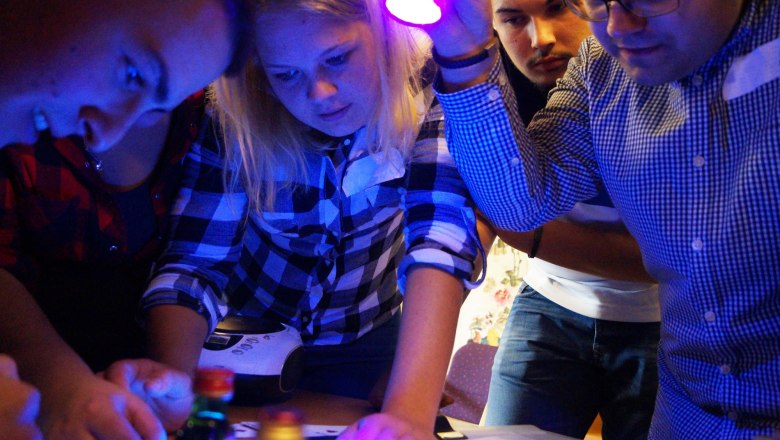 Gruppe von Menschen löst Rätsel in einem Escape Room mit UV-Licht.