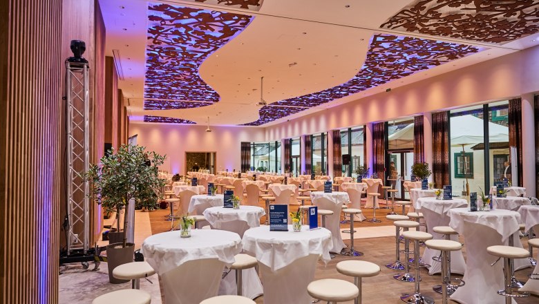 Innenansicht eines modernen Veranstaltungssaals mit dekorativer Decke und runden Tischen.