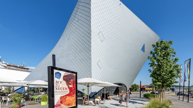 Moderne Architektur der Landesgalerie Niederösterreich in Krems mit Besuchern und Werbeplakat im Vordergrund.