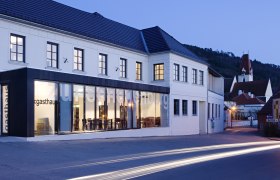 Au&szlig;enansicht des Gasthofs Hotel Zur Schonenburg bei D&auml;mmerung mit beleuchteten Fenstern und vorbeifahrenden Autos.