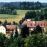 Ein gro&szlig;es Geb&auml;ude mit roten D&auml;chern in einer gr&uuml;nen, bewaldeten Landschaft.
