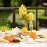 Frühstückstisch auf Terrasse mit Blumen, Saft, Brötchen und Eiern.