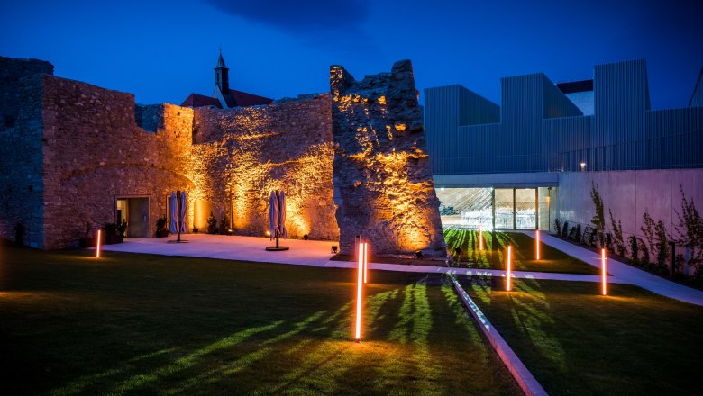 Beleuchtete Ruinen und moderne Architektur bei Nacht.