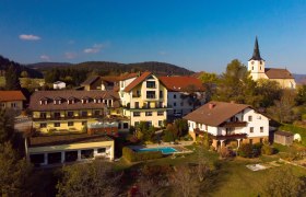 Luftaufnahme eines Dorfes mit einem Hotel, einem Pool und einer Kirche im Hintergrund.