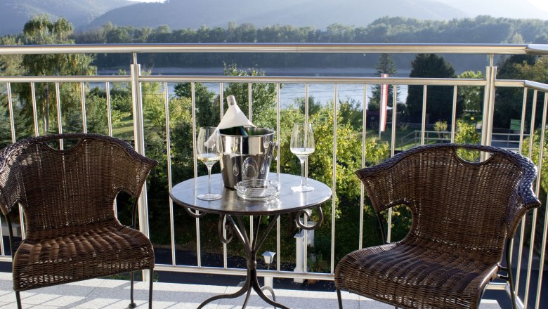 Zwei Rattanst&uuml;hle und ein Tisch mit Sektk&uuml;hler auf einer Terrasse mit Bergblick.