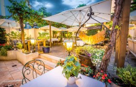 Gastgarten am Abend mit Beleuchtung und vielen Sitzmöglichkeiten, Pflanzen und Schirmen.