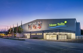 Außenansicht der Messe Tulln bei Dämmerung mit beleuchtetem Eingang und Fahnen.