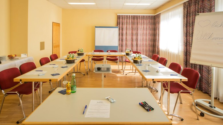 Seminarraum mit U-f&ouml;rmiger Tischanordnung, Flipchart und Getr&auml;nken.
