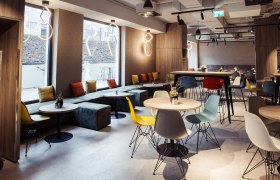 Modernes Hotel-Restaurant mit bunten St&uuml;hlen und Tischen, gro&szlig;en Fenstern und stilvollen Leuchten.