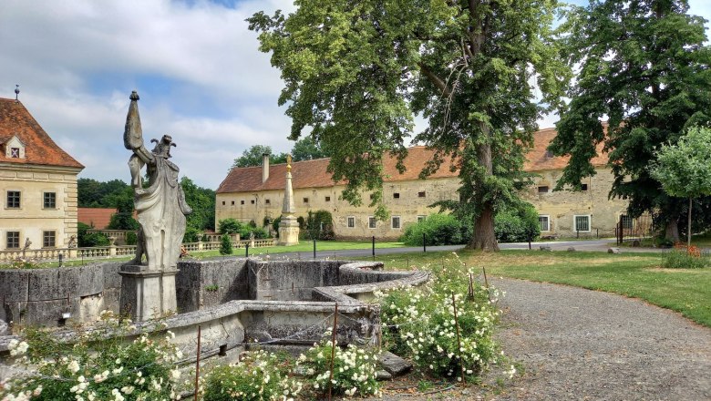Blick auf eine historische Schlossanlage mit Statue und Garten.