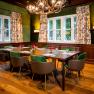 Ein Jagdzimmer mit Holztisch, gr&uuml;nen St&uuml;hlen und Geweihleuchter.