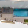 Draufsicht auf einen rechteckigen Pool mit Liegest&uuml;hlen und Tischen auf einer gefliesten Terrasse.