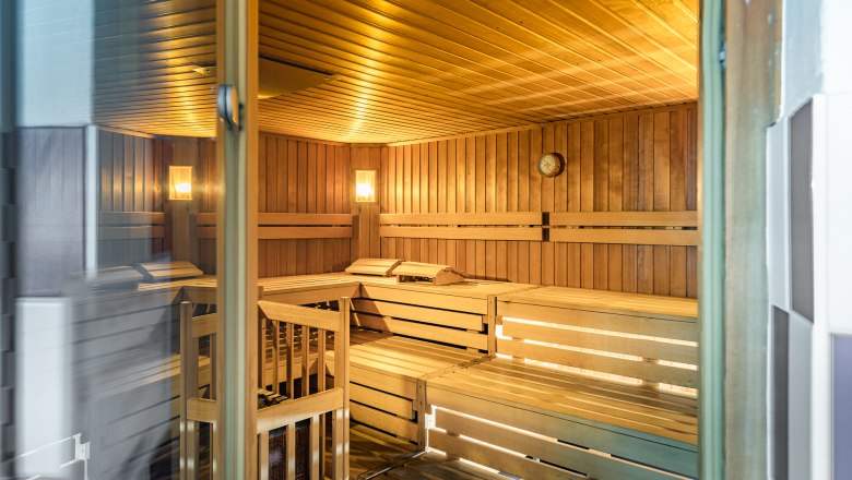 Innenansicht einer leeren Sauna mit Holzb&auml;nken und Wanduhr.