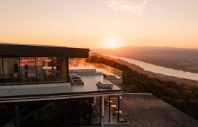 Modernes Hotel mit Terrasse und Flussblick bei Sonnenuntergang und Blick &uuml;ber die Donau.