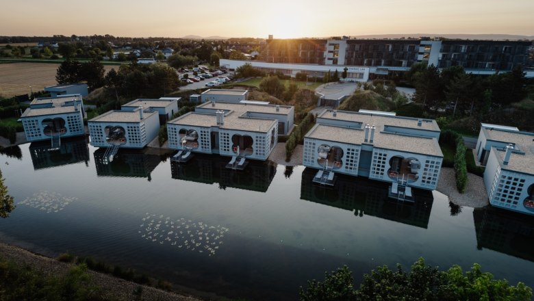 Luftaufnahme von modernen Geb&auml;uden am Wasser im Thermenresort Laa bei Sonnenuntergang.