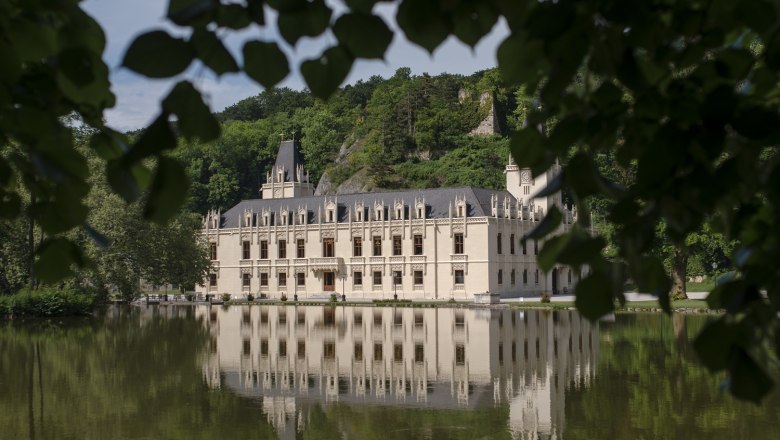 Schloss Hernstein spiegelt sich in einem See, umgeben von Bäumen.
