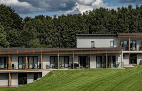 Modernes Hotelgebäude mit Terrasse vor einem Wald.