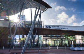 Eingang des Museums Niederösterreich mit moderner Architektur und Sonnenstrahlen.
