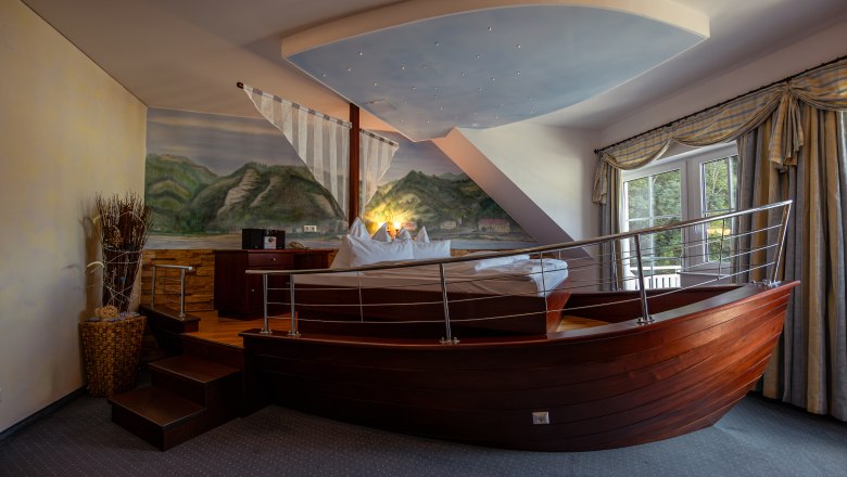 Hotelzimmer mit Bett in Form eines Bootes, Wandgem&auml;lde von Landschaft, Fenster mit Vorh&auml;ngen.
