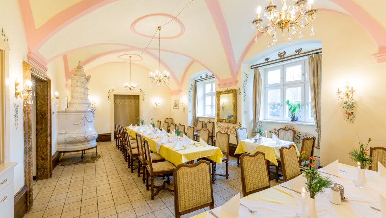 Eleganter Speisesaal mit gedeckten Tischen, Kronleuchtern und Kachelofen.