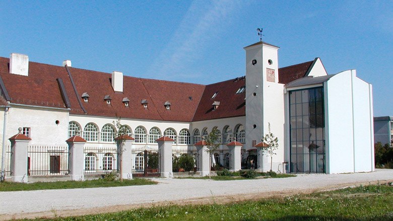 Schloss Katzelsdorf mit modernem Anbau und historischem Geb&auml;ude. Wei&szlig;e Fassade mit gerundeten Fenstern, rotes Dach und gro&szlig;er Innenhof