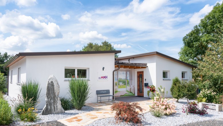 Modernes, weißes Gebäude mit Garten und Kiesweg, blauer Himmel im Hintergrund.