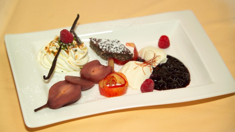 Ein Dessertteller mit verschiedenen S&uuml;&szlig;speisen, darunter Sahne, Beeren, Schokoladenkuchen und pochierte Birnen.