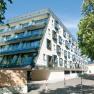 Modernes Hotelgebäude mit Glasbalkonen und Bäumen im Vordergrund.
