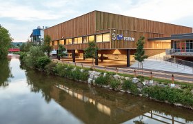 Modernes Gebäude der Messe Wieselburg mit Holzfassade und Fluss im Vordergrund.