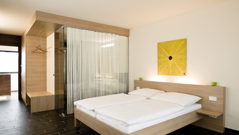 Modernes Hotelzimmer mit Doppelbett, Holzm&ouml;beln und gelbem Kunstwerk an der Wand.