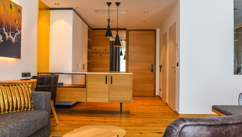 Innenansicht einer modernen Hotelsuite mit Holzboden, grauem Sofa und hölzernem Schreibtisch.