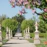 Ein gepflegter Gartenweg mit Statuen und bl&uuml;henden B&auml;umen im Fr&uuml;hling.