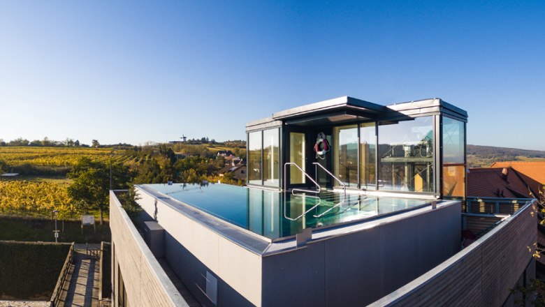 Dachpool mit Glasw&auml;nden auf einem modernen Geb&auml;ude, umgeben von Landschaft.