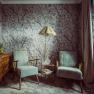 Ein stilvoll eingerichtetes Zimmer mit zwei blauen Sesseln, einer Stehlampe und einer Kommode mit Blumen und einer Uhr.