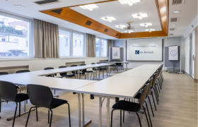 Seminarraum im Das Reinisch Hotel mit Tischen, Stühlen und Präsentationsleinwand.